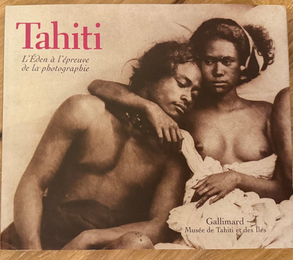 A book titled 'Tahiti' lying flat on a light brown wooden surface. The cover features a vintage-style sepia-toned photograph of two nude figures, with the title in red and subtitle text in black.
